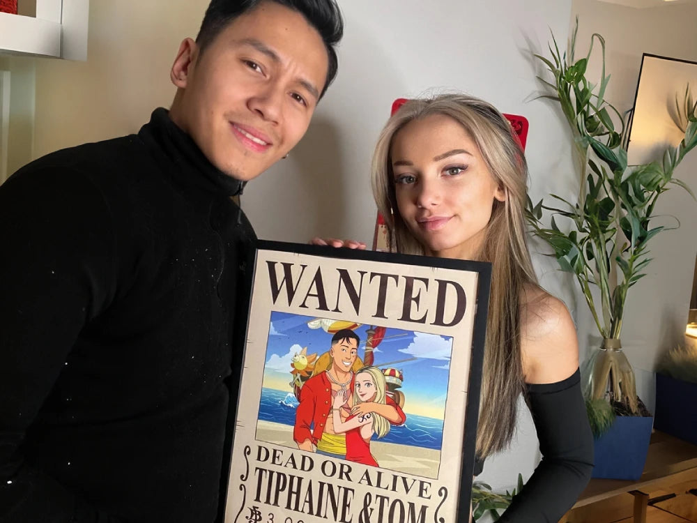 Un couple souriant tient une illustration personnalisée encadrée d'une affiche Wanted inspirée du manga One Piece. L’homme y est caricaturé en Luffy et la femme en Nami, avec le Thousand Sunny en arrière-plan.